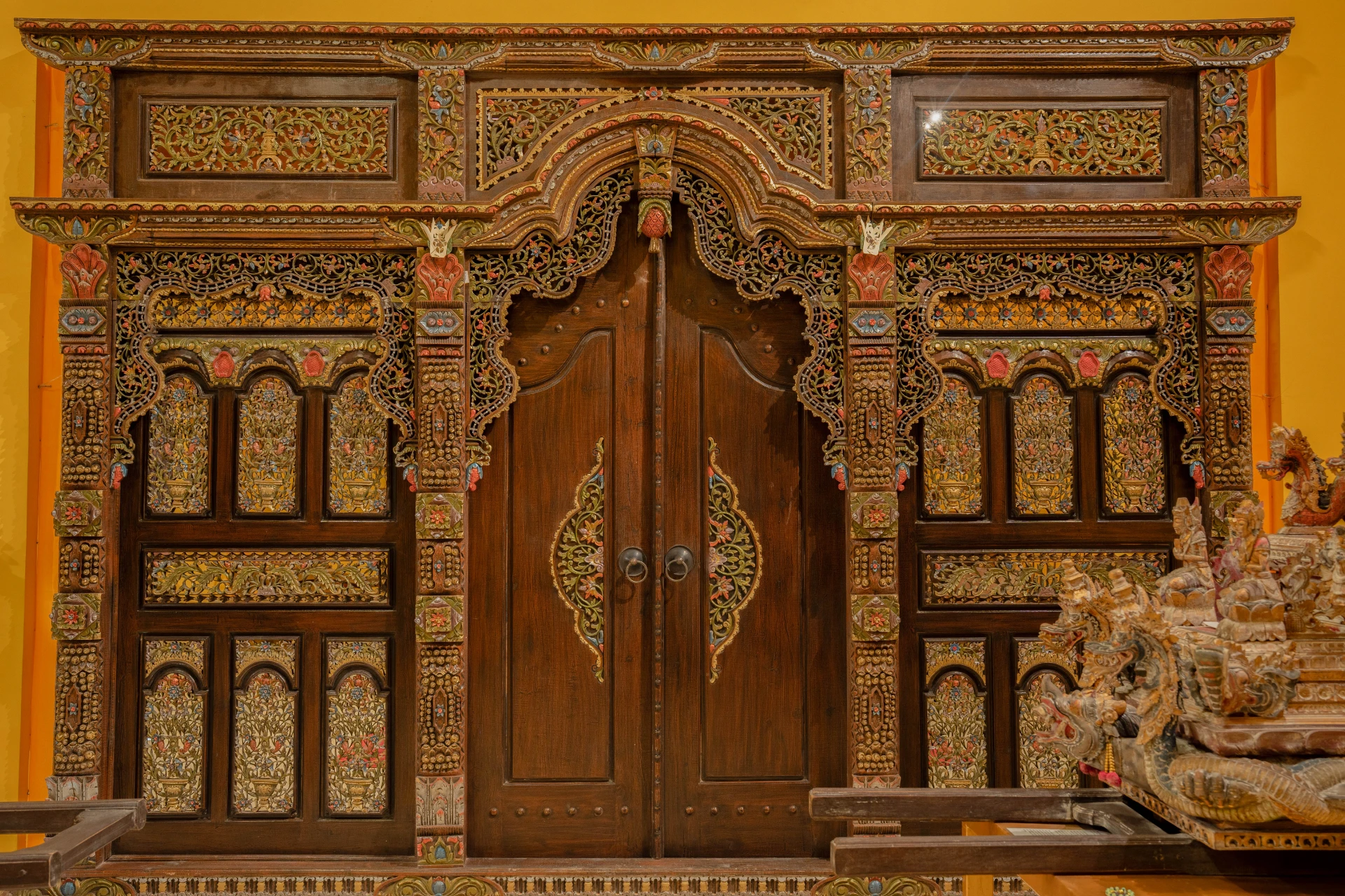 Traditional Balinese carved wooden doorway with intricate ornaments and ceremonial textiles, Annemarie Kipar Room.