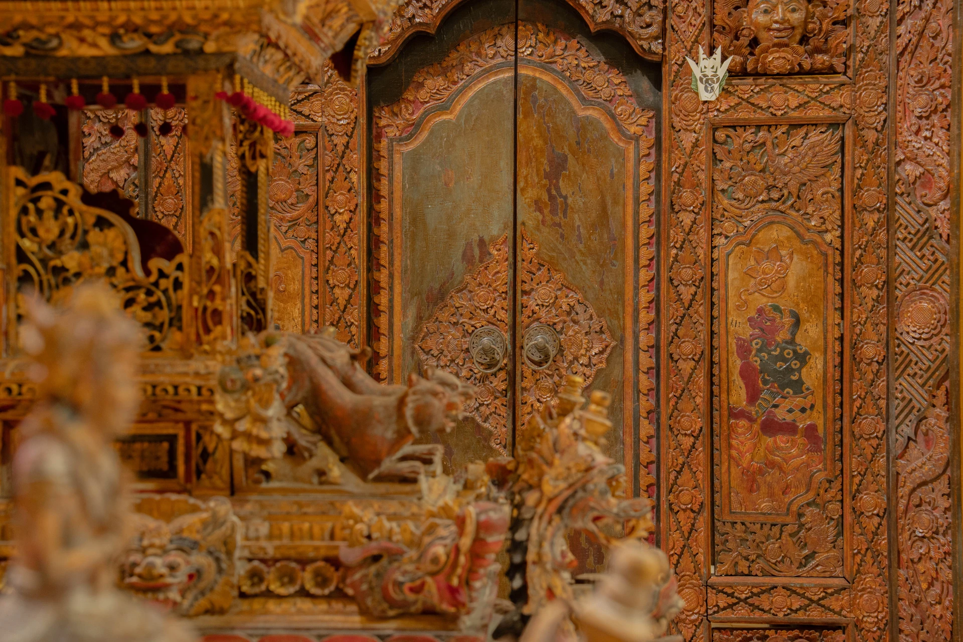 Traditional Balinese carved wooden doorway with intricate ornaments and ceremonial textiles, Annemarie Kipar Room.