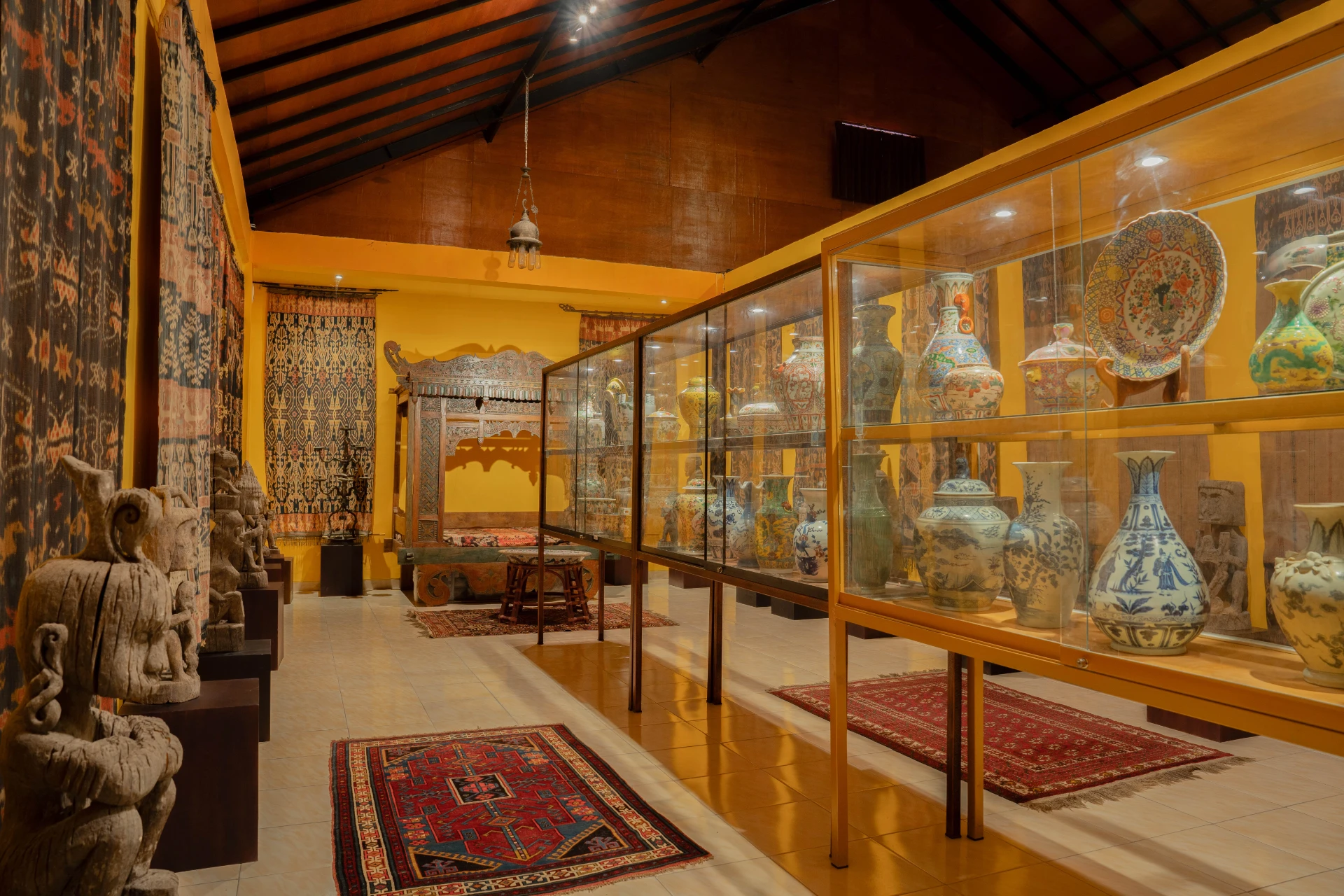 Glass display featuring traditional Balinese textiles and carved wooden structures.