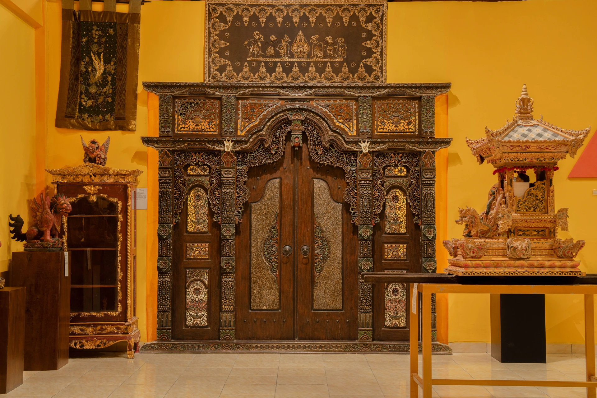 Traditional Balinese carved wooden doorway with intricate ornaments and ceremonial textiles, Annemarie Kipar Room.